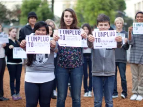 Children and Adults Holding Signs that Say I Unplug To
