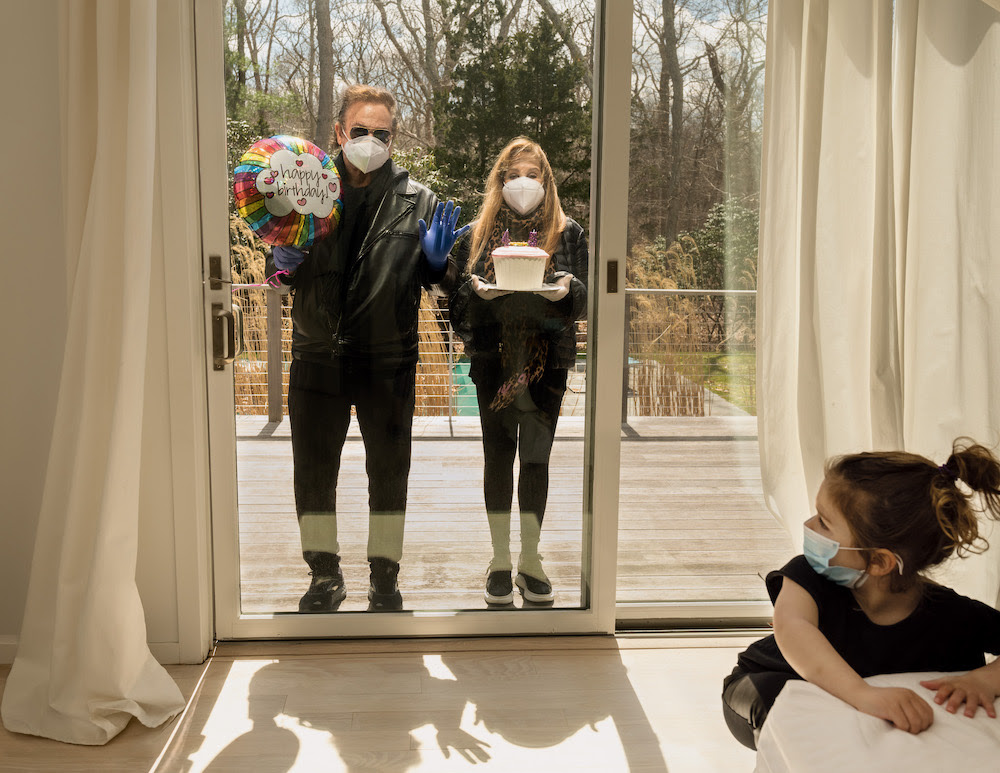 Two people stand in masks outside a sliding glass door in "My quarantine birthday" by Gillian Laub, 2020