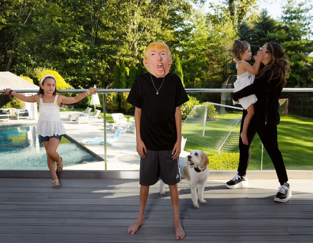 Boy wearing a trump mask with family in the background. For Family Matters by Gillian Laub